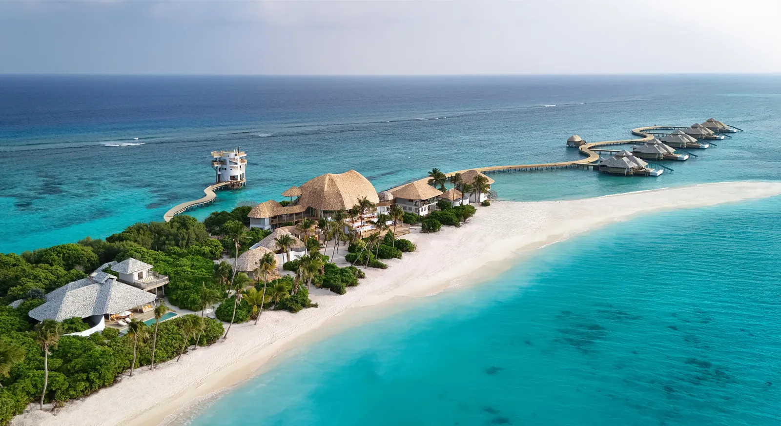 Dhipparufushi from above: villas among the trees, the long beach and the jetties out to the water villas and the tower.