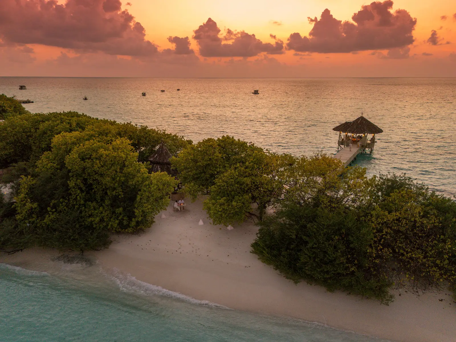 The island’s shore at sunset, with low greenery, the beach and a pavilion over the water.