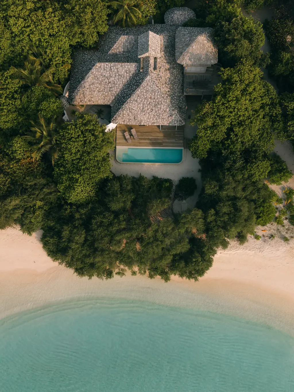 A One-Bedroom Beach Villa from above: its shingle roof among the trees, the pool and the beach in front.