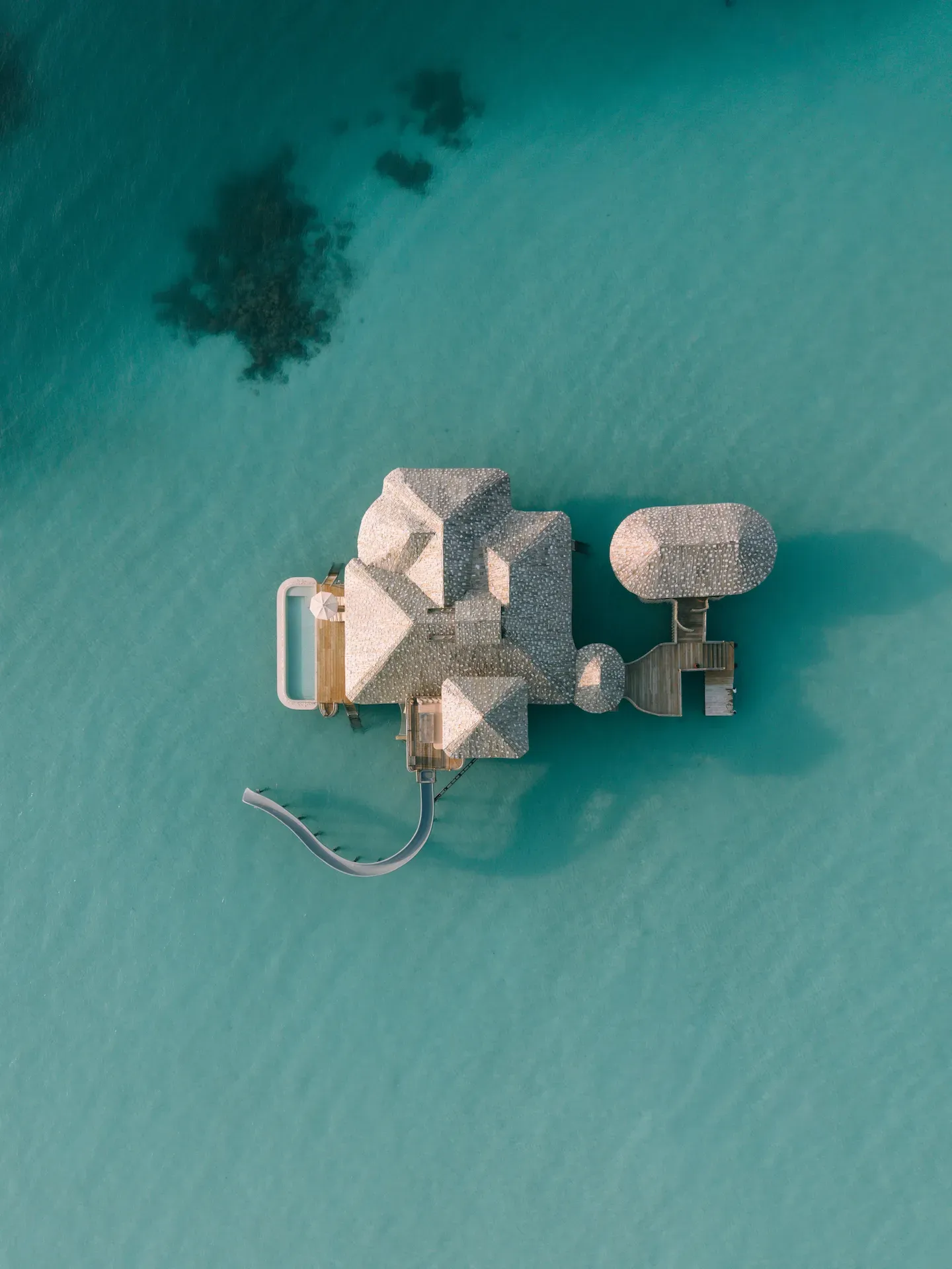 A One-Bedroom Overwater Sea Loft from directly above, alone in the lagoon, with its pool and slide.