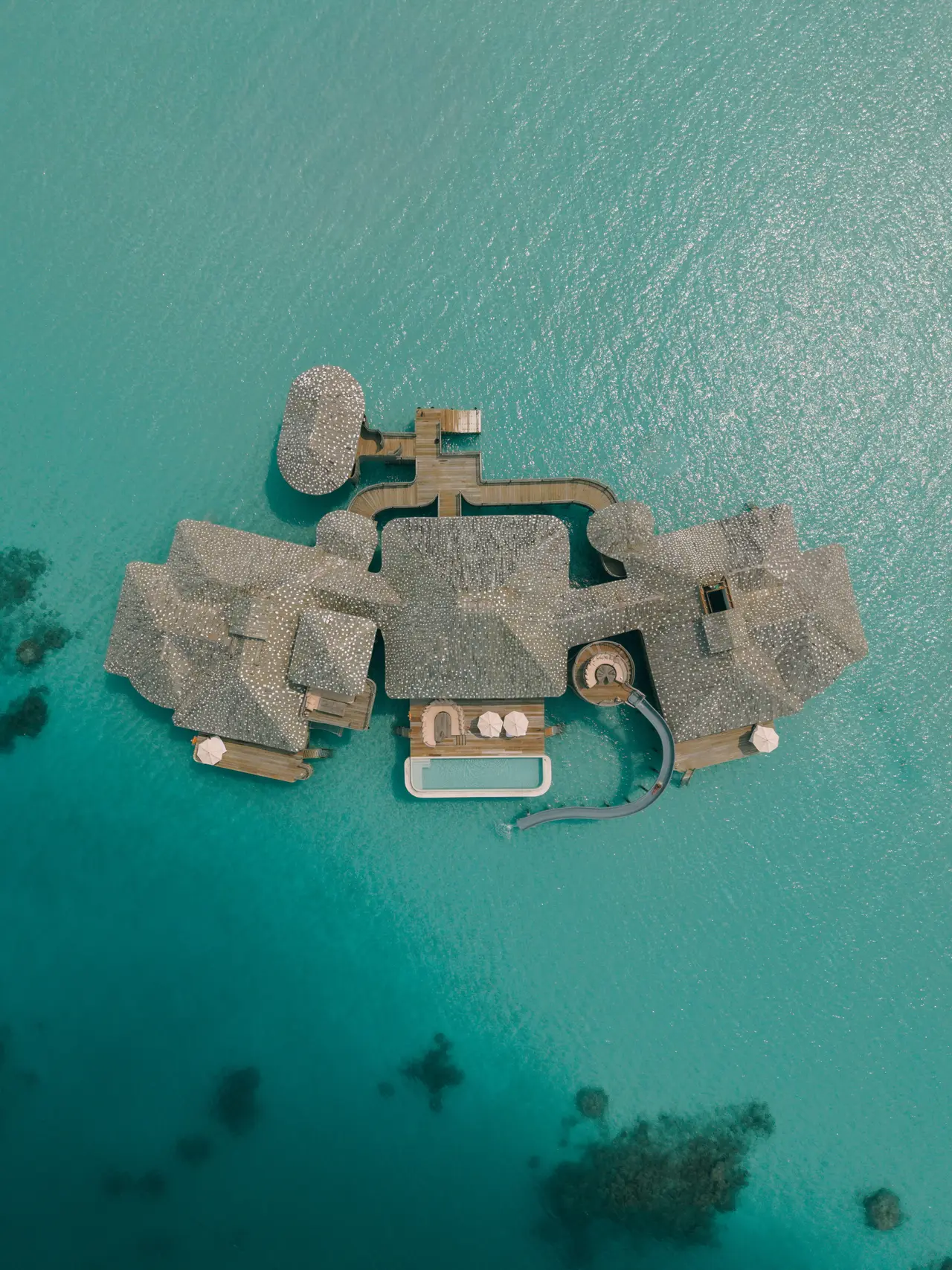 A Two-Bedroom Overwater Sea Loft from above: its roofs, pool and walkways in the middle of the lagoon.