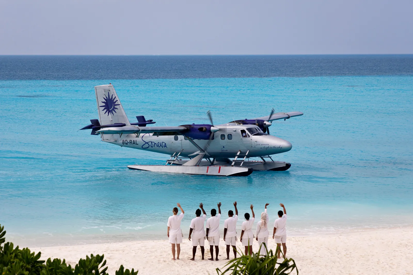 Soneva’s seaplane resting on the lagoon and, on the beach, staff in white waving with their arms raised.