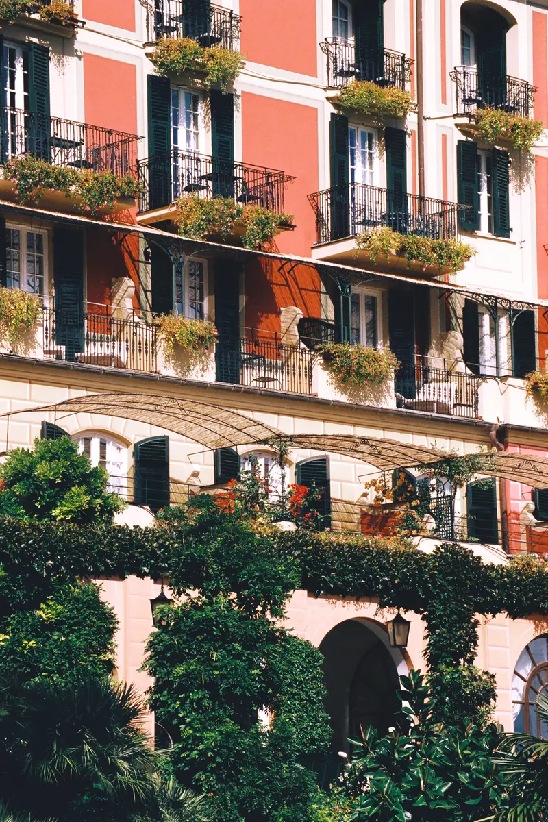 The pink façade with green shutters, flowering iron balconies and climbers over the ground-floor arches.