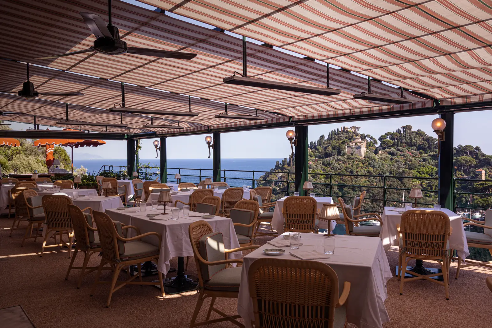 The Splendido Grill’s terrace under its striped awning, tables laid, the headland beyond the railing.