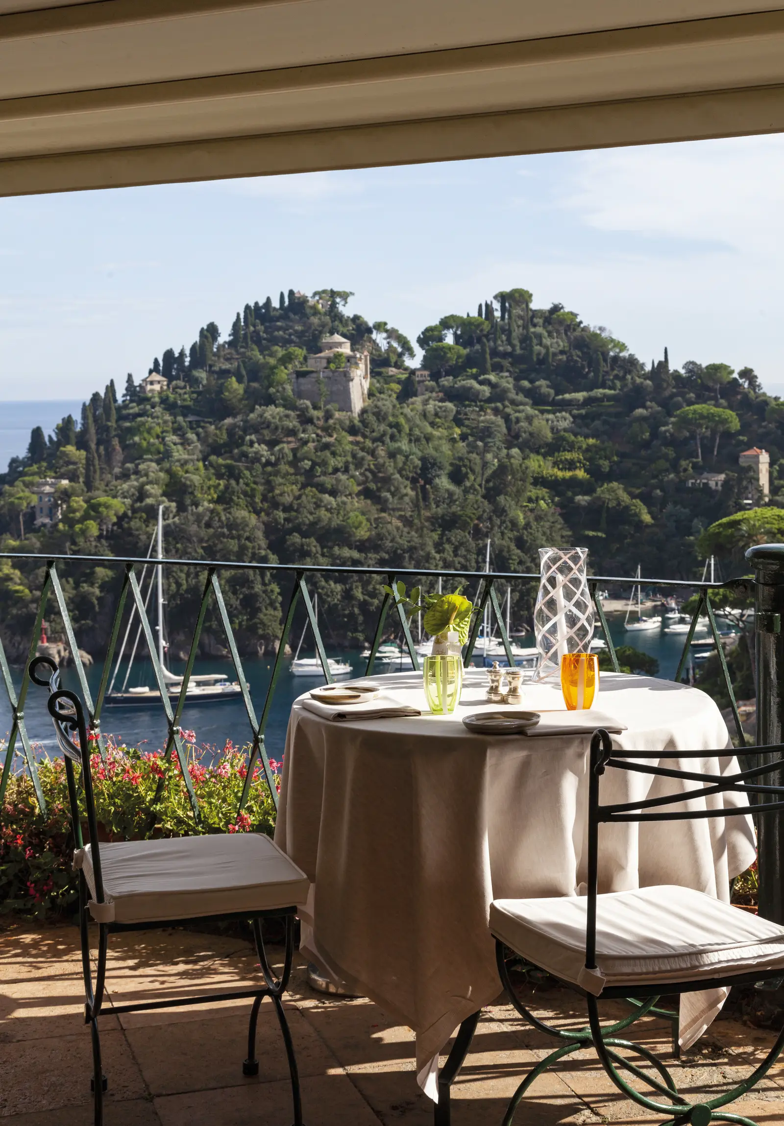 A table for 2 on La Terrazza’s terrace, against the railing, with sailing boats in the bay and the headland.