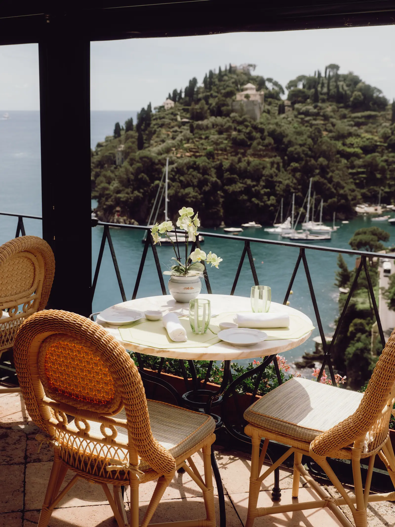 A laid table with wicker chairs on the restaurant’s terrace, the bay and the headland behind.