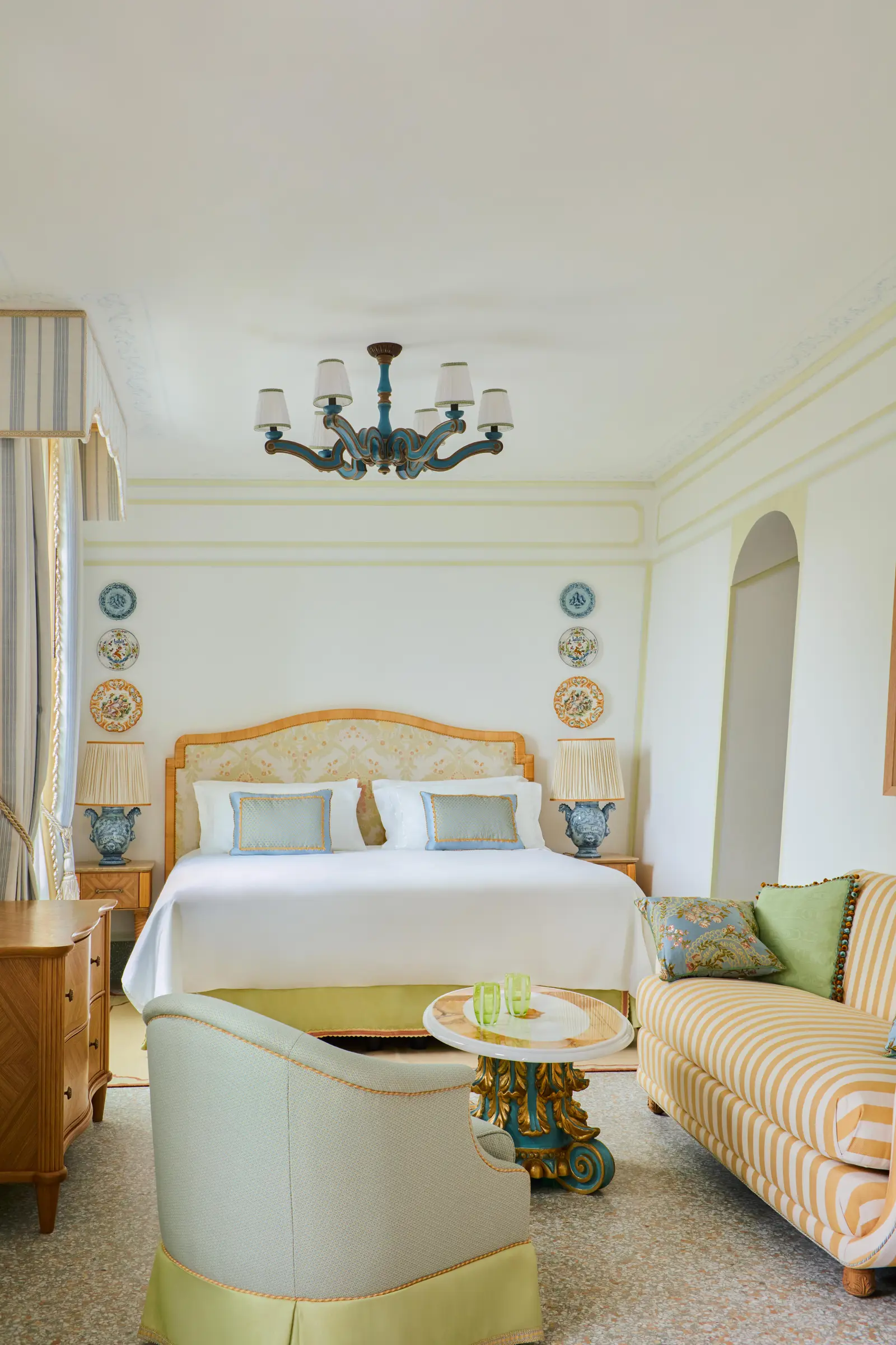 The Baratta Junior Suite: the bed between 2 blue ceramic vases, the yellow-striped sofa and a gilded table.