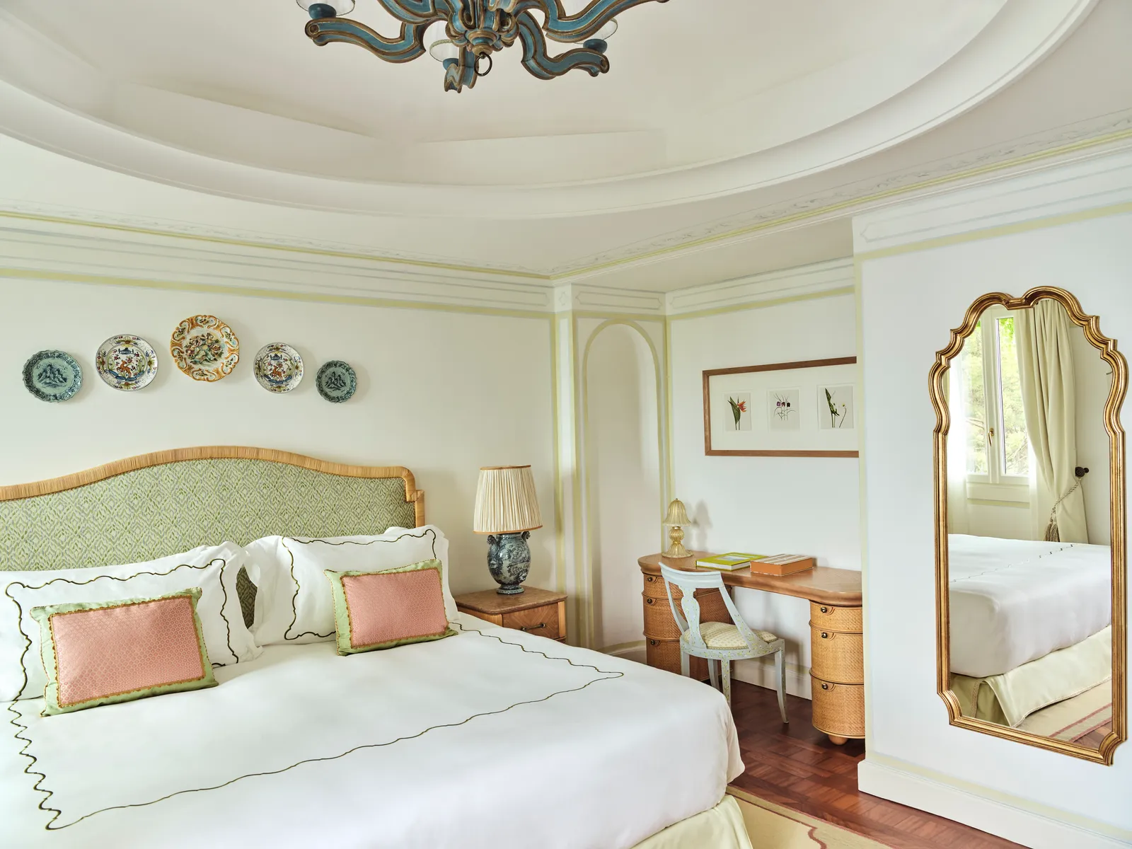 A Heritage Garden View room: the bed with its green headboard, ceramic plates on the wall and a gilded mirror.
