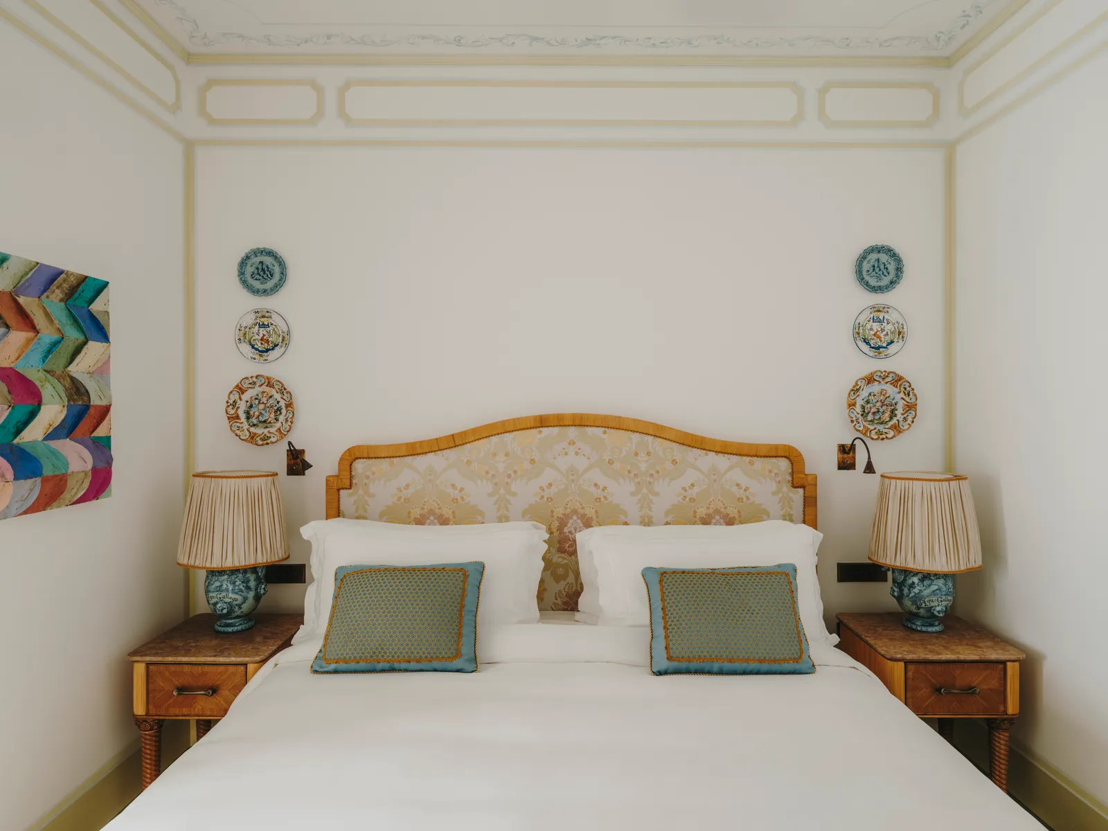 A Prestige Junior Suite: the bed with its woven headboard between 2 ceramic lamps, plates on the walls.