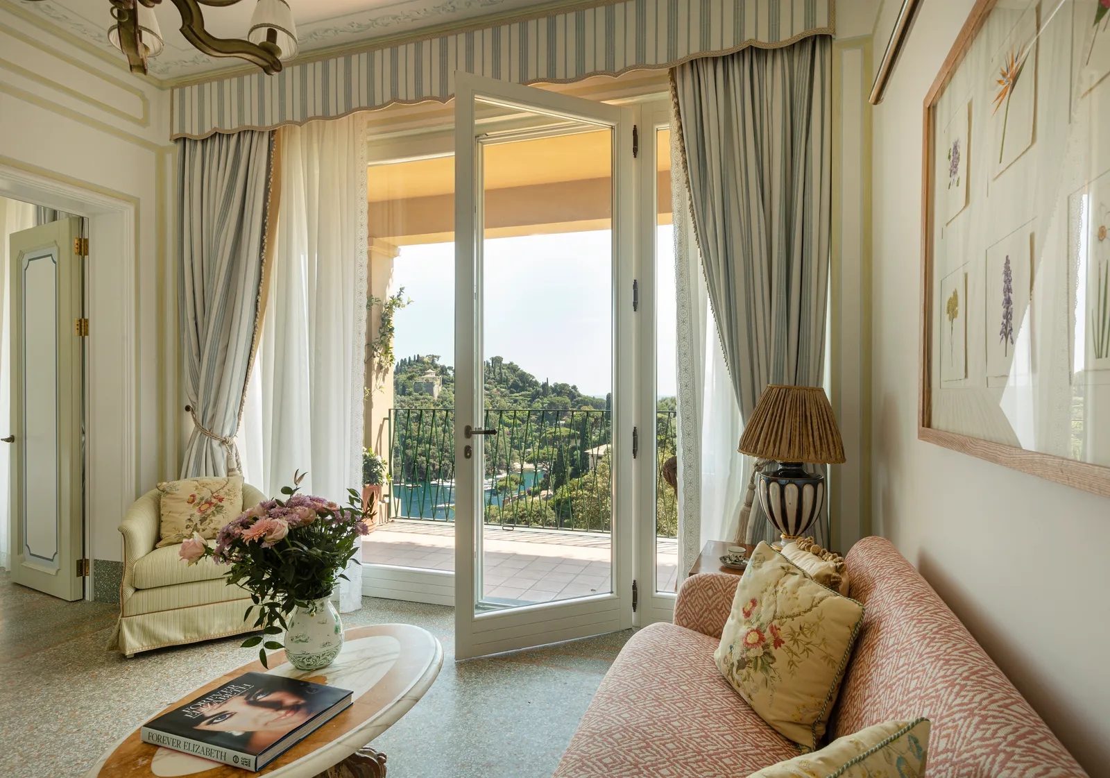 A Prestige Suite’s sitting room, with the pink sofa, flowers on the table and the French window onto the terrace and the bay.