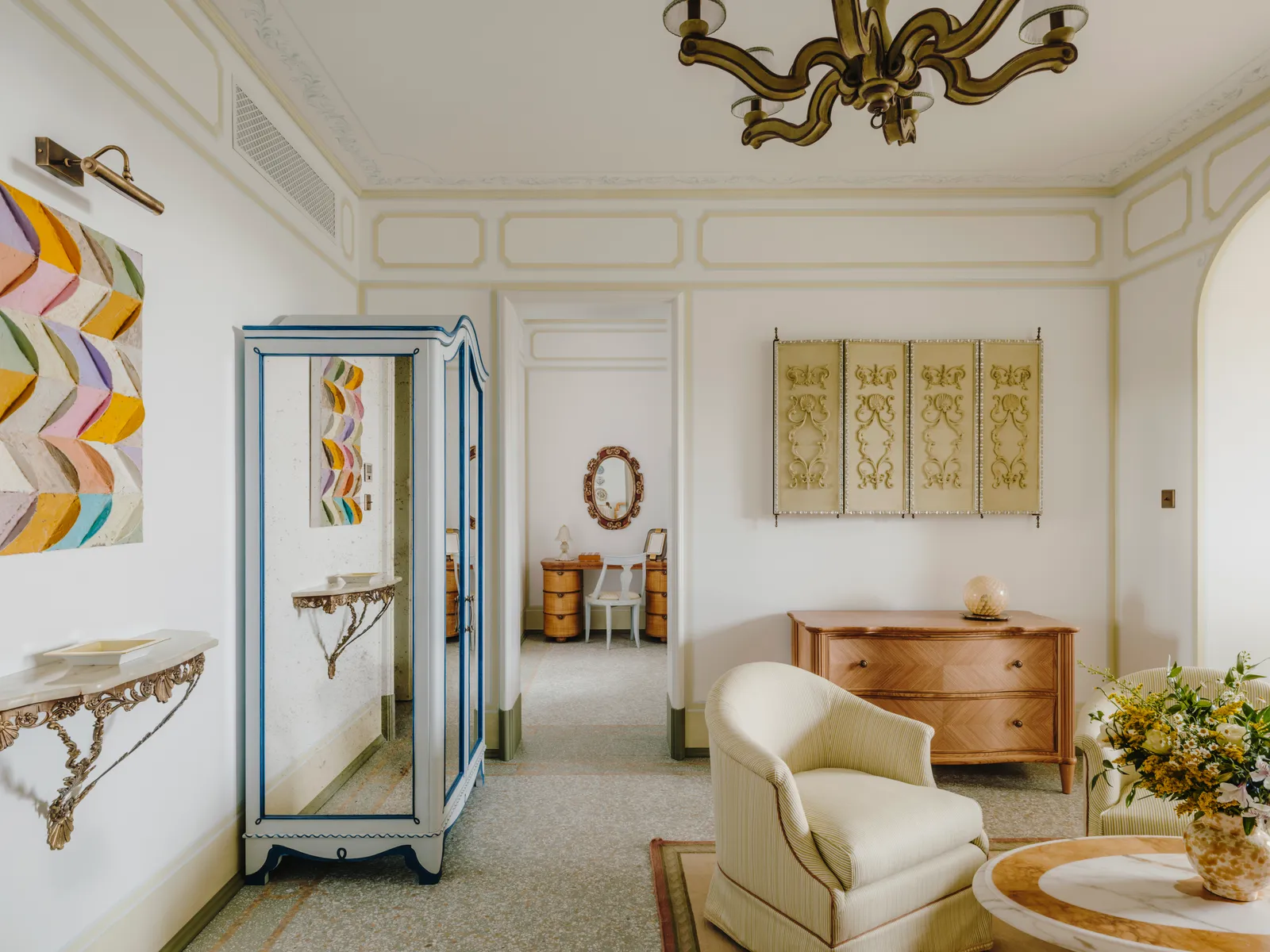 A Riviera Suite’s living room: the pale armchair, the chest of drawers and a painted cabinet between white walls.