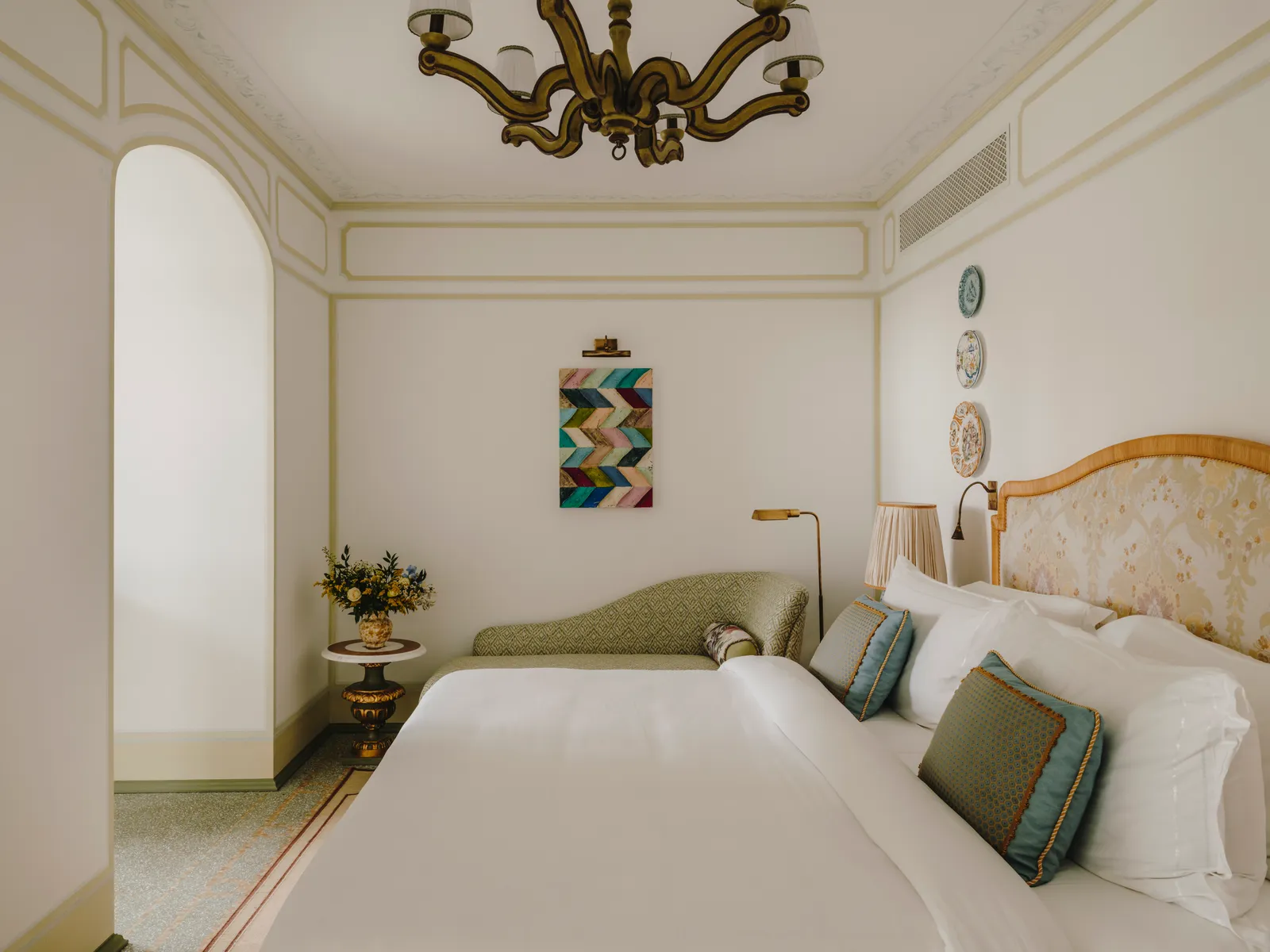 A Smeraldo Junior Suite: the bed, the green chaise at its foot and a geometric painting on the wall.