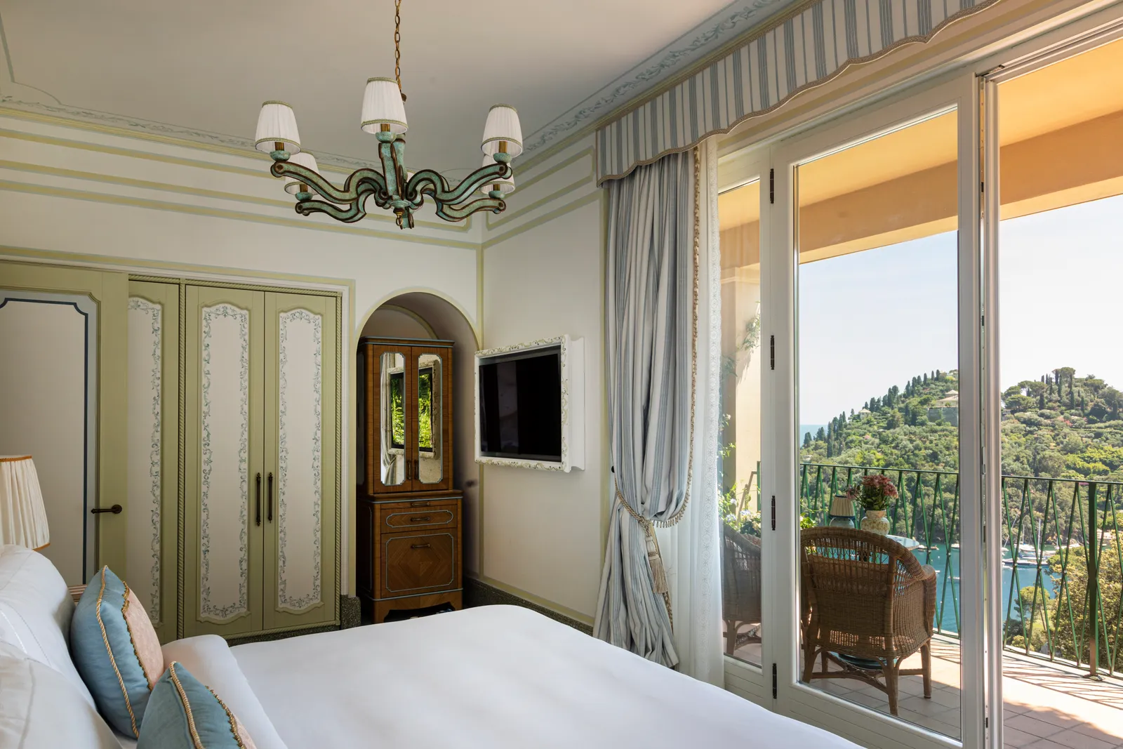 A Premium Room: the white bed in front, French windows open onto the terrace and the headland over the bay.
