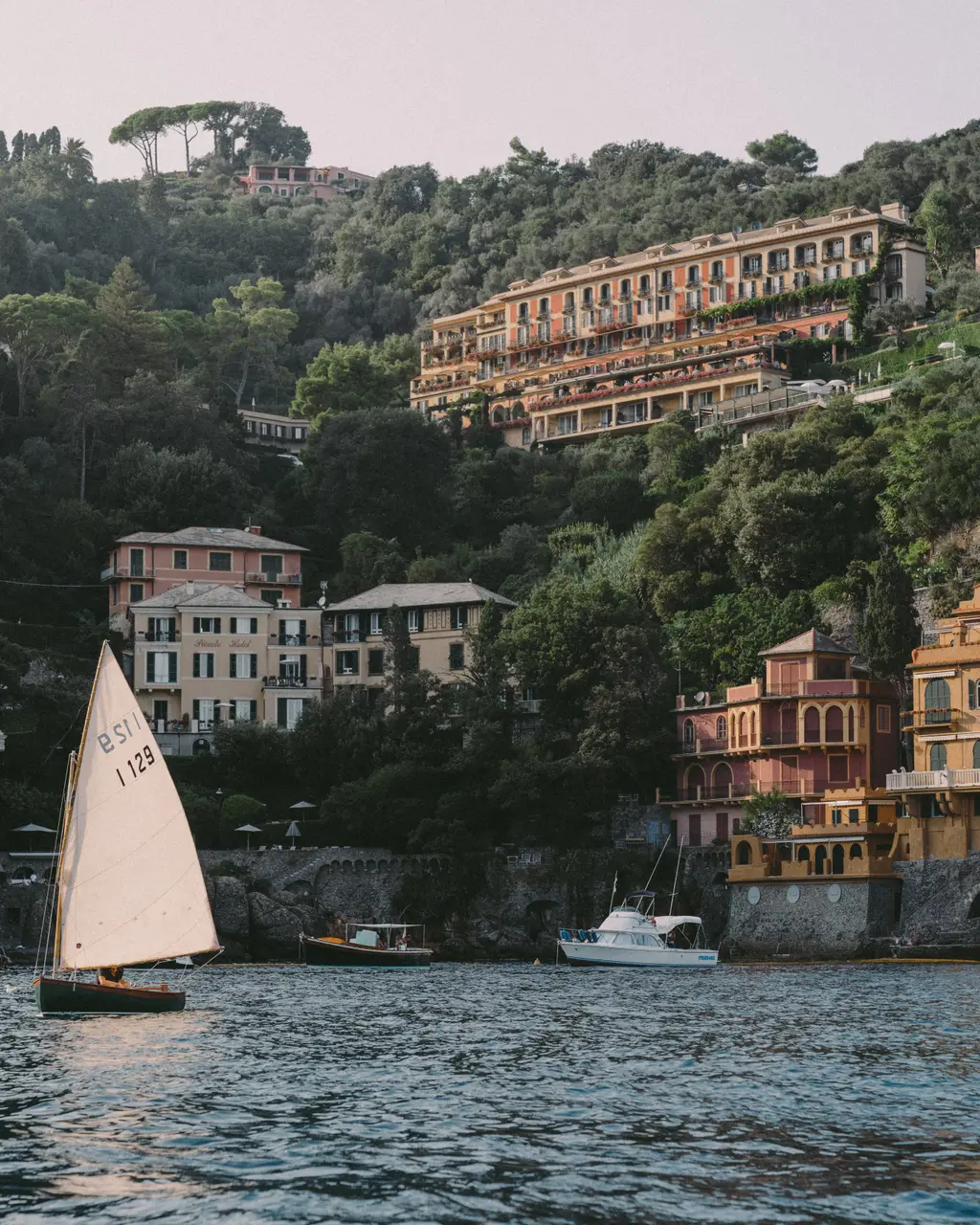 Splendido high on the hill seen from the sea, above Portofino’s painted houses, a sailing boat in front.