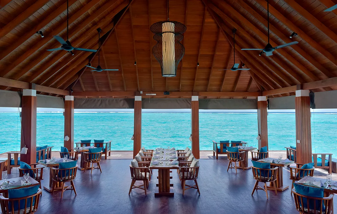 Wooden tables under an open shelter overlooking the sea.