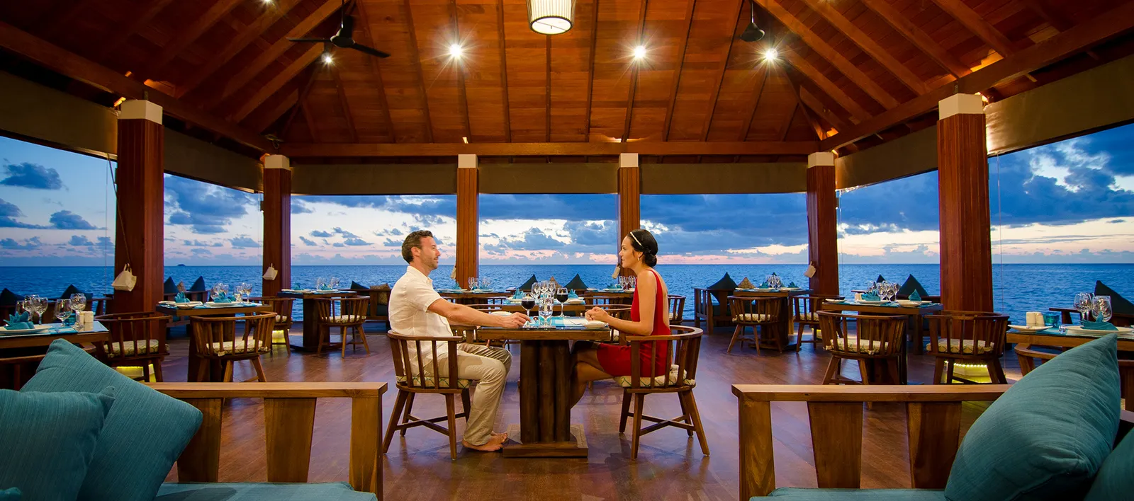 A couple dining in a restaurant overlooking the sea at dusk.