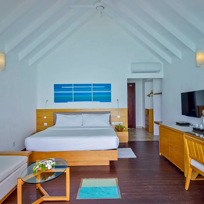 The Water Villa bedroom with a bed, sofa and glass floor panel.