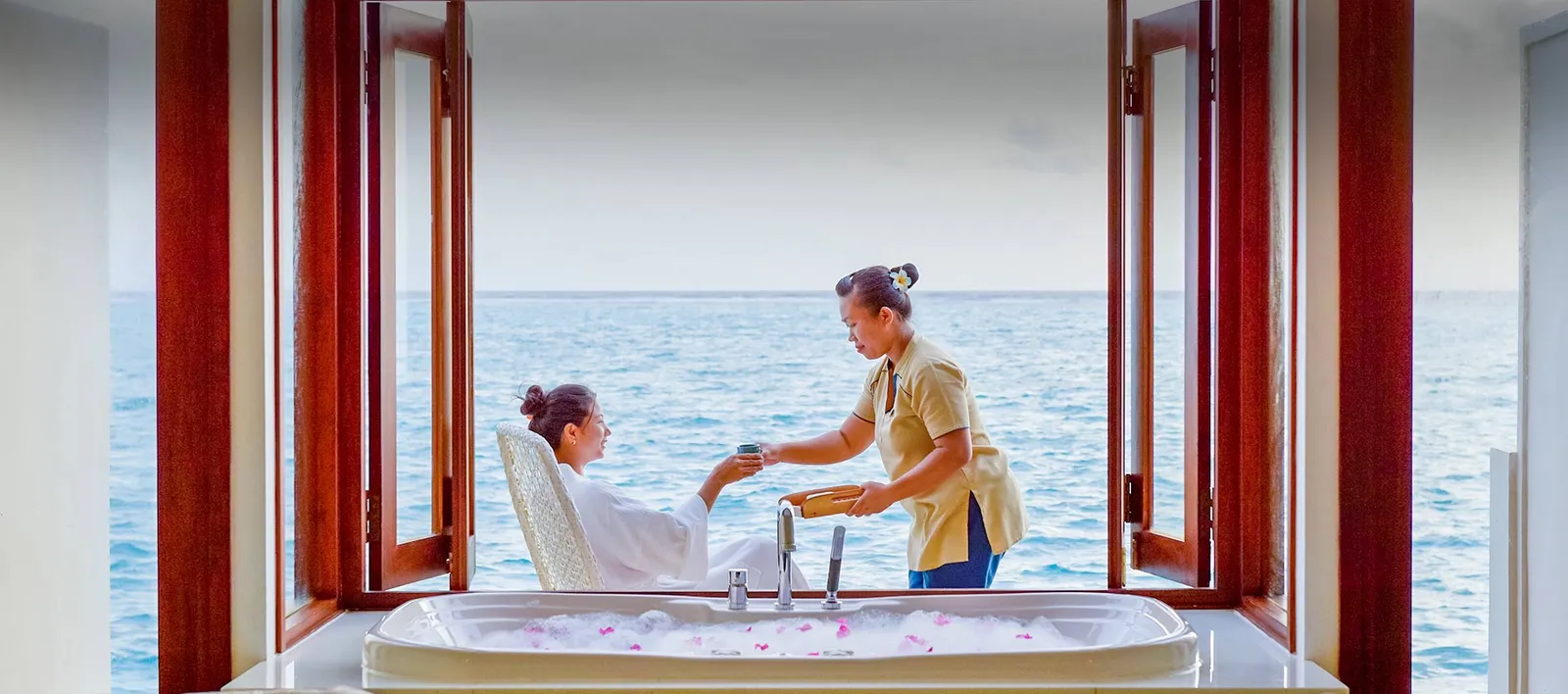A woman in a robe receiving a drink on the spa terrace.