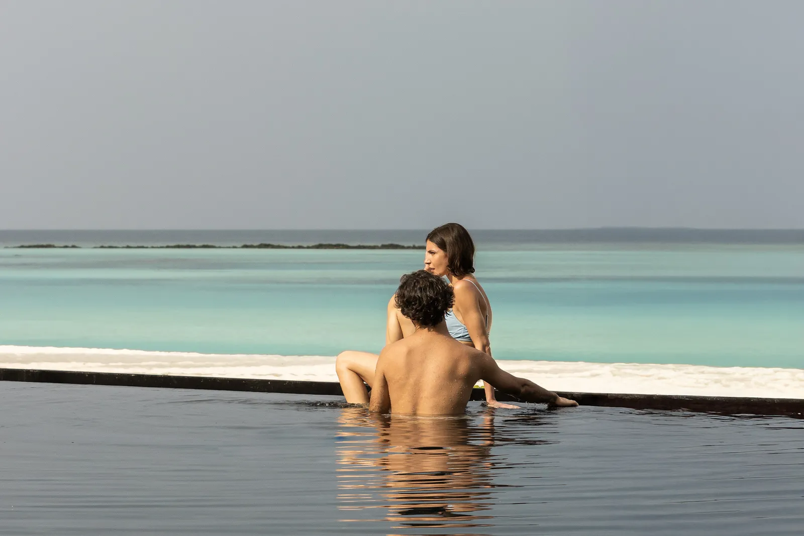 A couple at the edge of an infinity pool that merges into the lagoon.