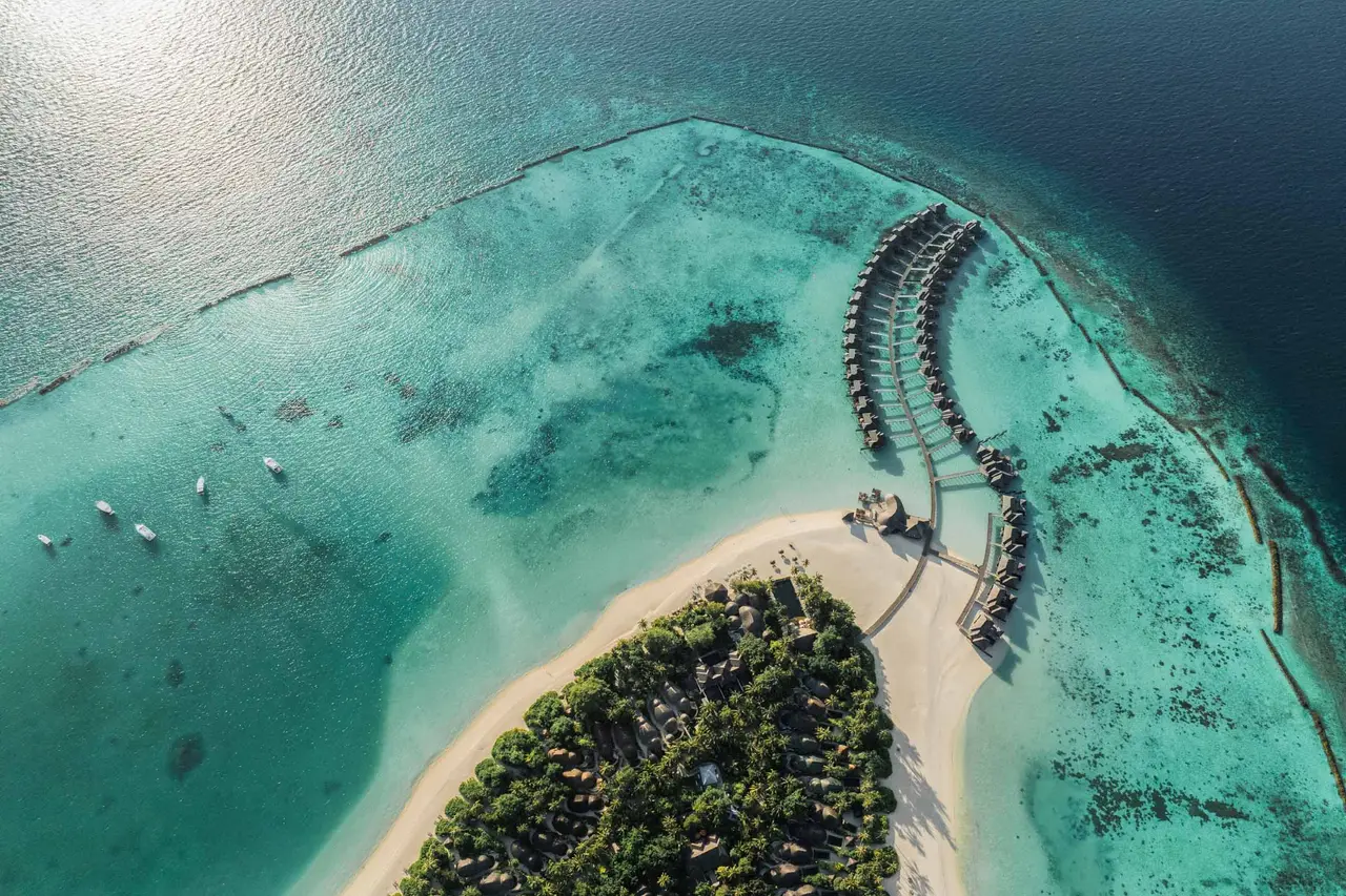 One tip of Iru Fushi from above: the white beach, the woods and the curved row of water villas.