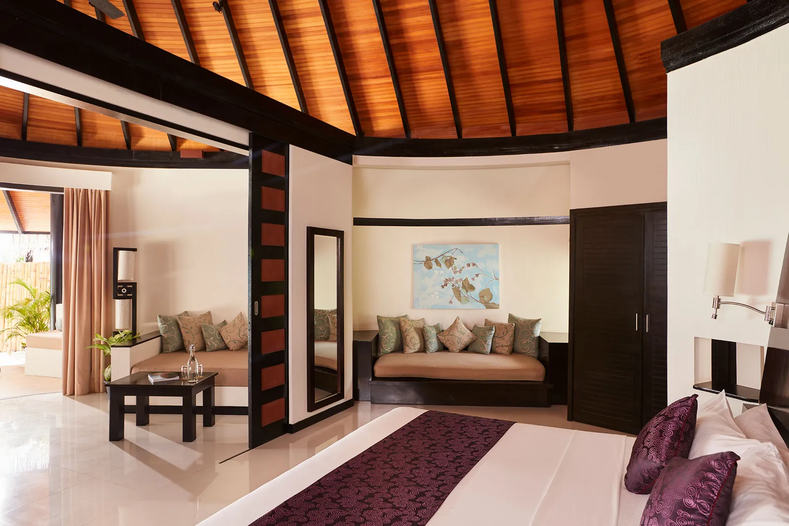 Inside a Family Deluxe Beach Villa with Pool: the large bed, the sitting area with its sofa and the timber ceiling.