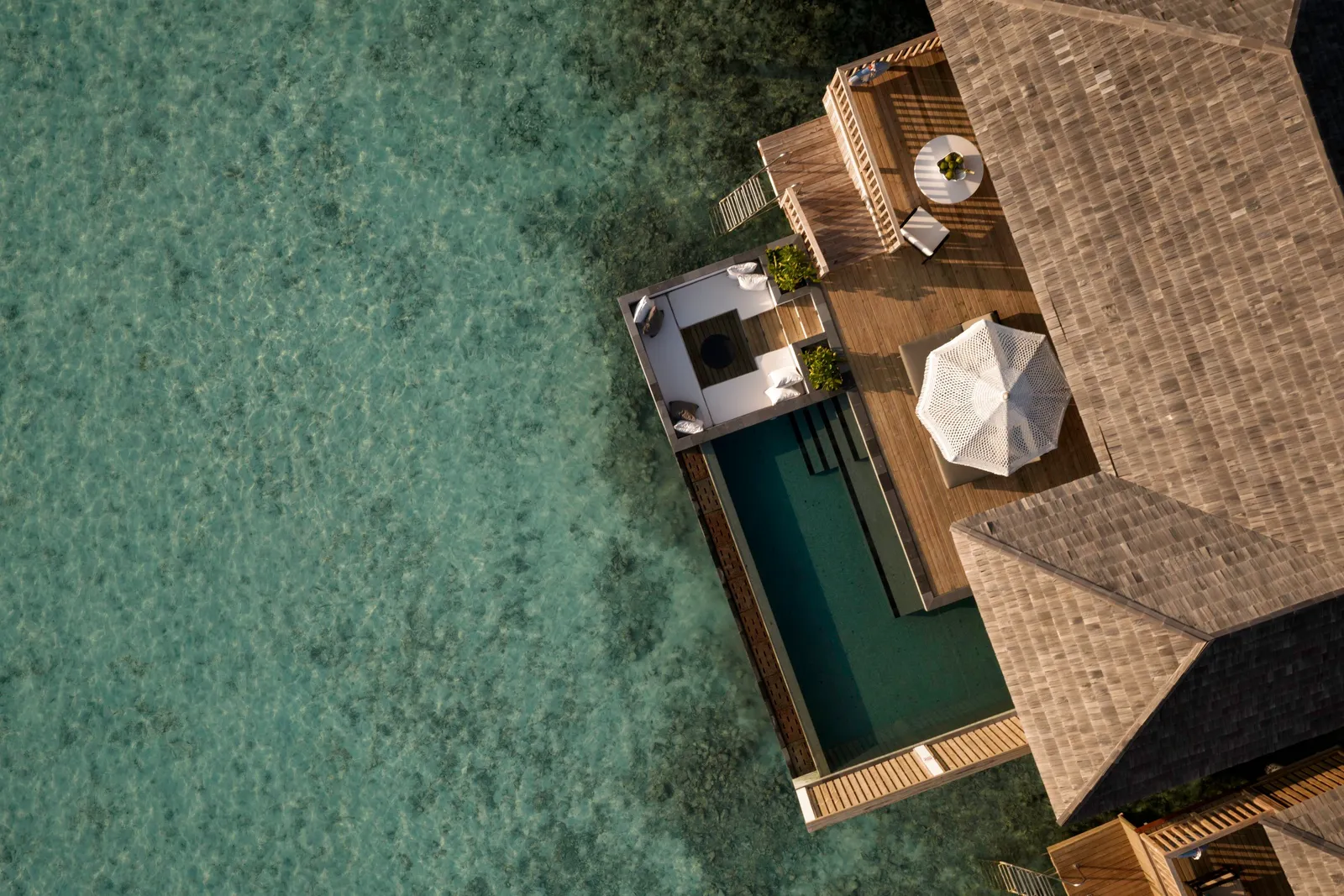 A Sunset Horizon Water Villa with Pool seen straight down: the roof, the pool and the deck over green water.
