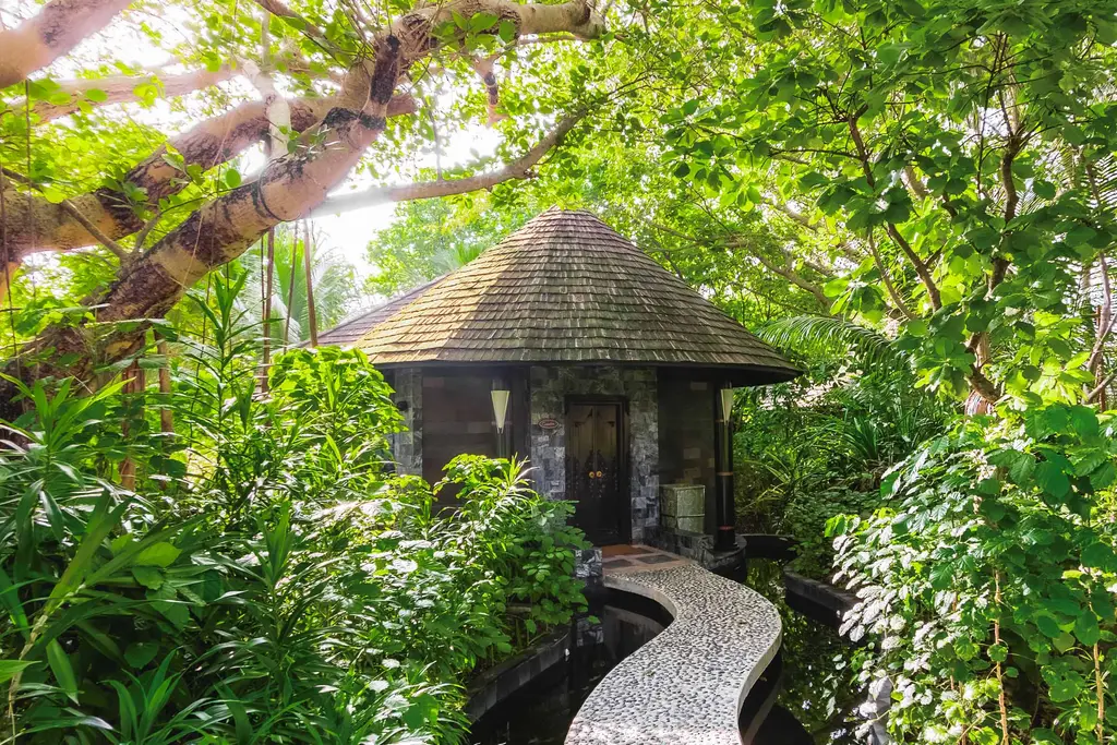 A spa pavilion in dense greenery, with the pebbled path crossing the water.