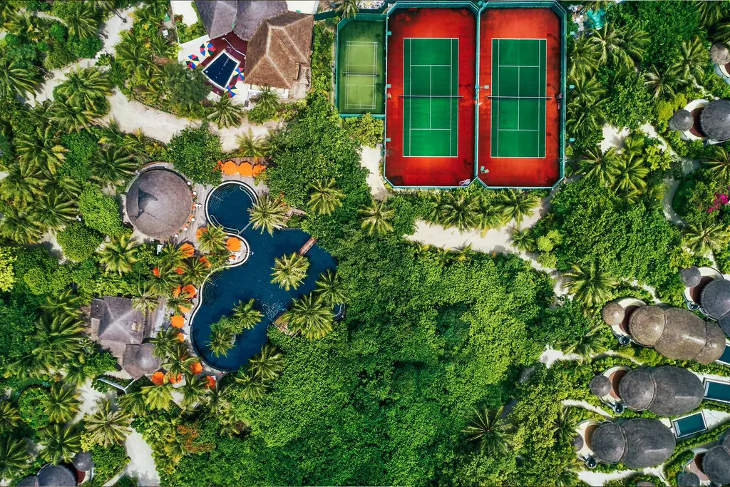 The tennis courts from above, in the island’s greenery, beside the villa roofs.