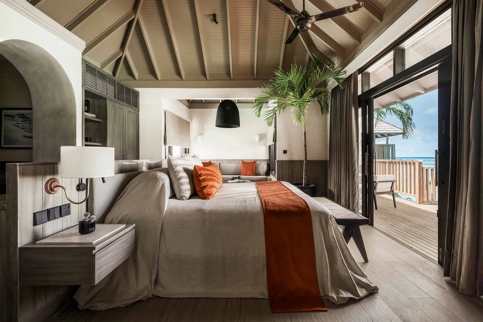 The bedroom of a Water Villa with Pool: the bed facing the deck, the timber ceiling and the glass doors open to the sea.