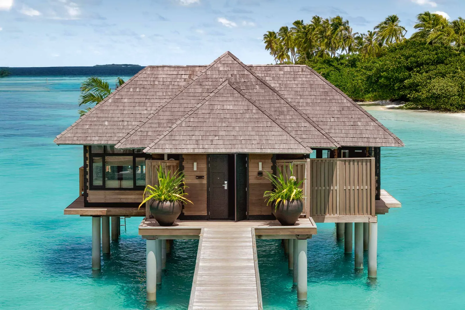 A Water Villa with Pool on stilts in the turquoise lagoon, with the timber walkway leading to its door.