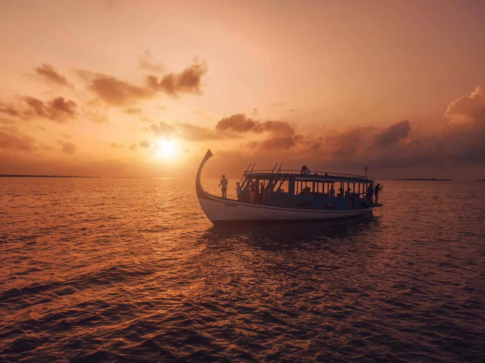 A traditional dhoni under way at sunset on an orange sea.