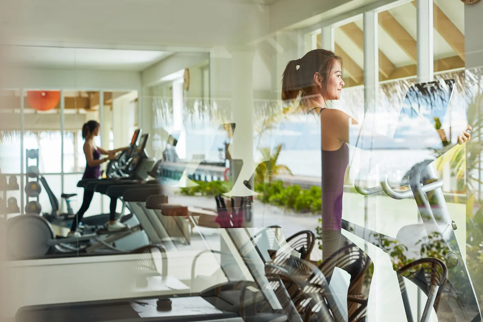 The gym with its windows on the sea, a guest on a treadmill and the machines in a row.