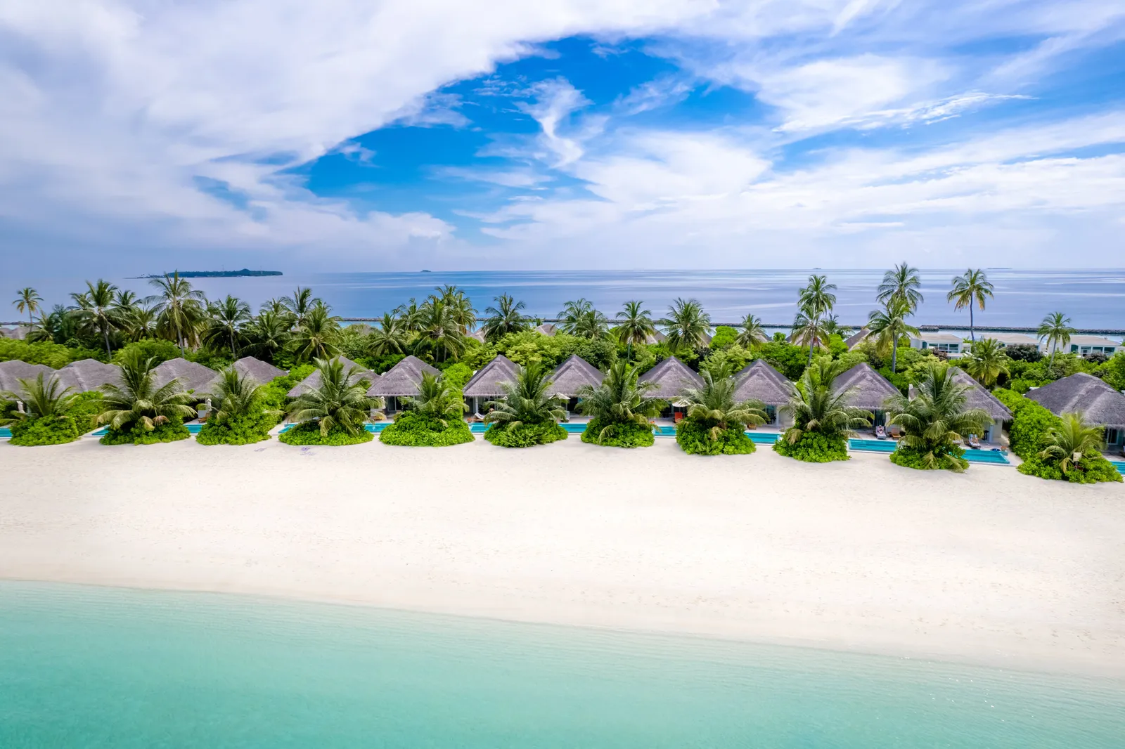 The beach villas in a row among the palms, facing the white sand and the pale lagoon.