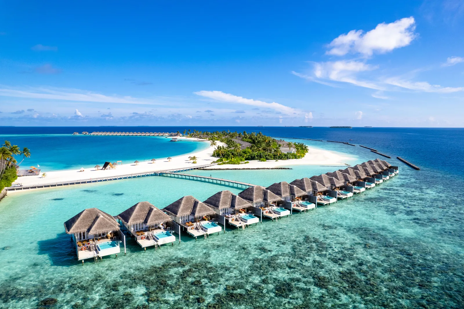 Iru Veli from above: the row of water villas on the turquoise lagoon, the spit of white sand and the green island behind.