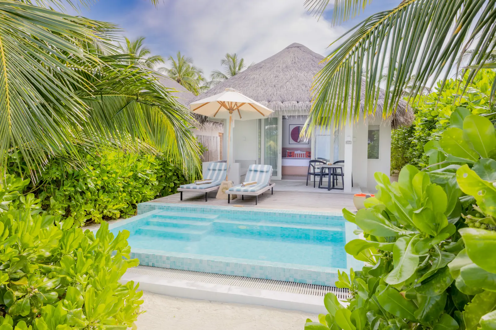 A Beach Villa with Pool: the pool in front of the thatched villa, with loungers and palms around it.