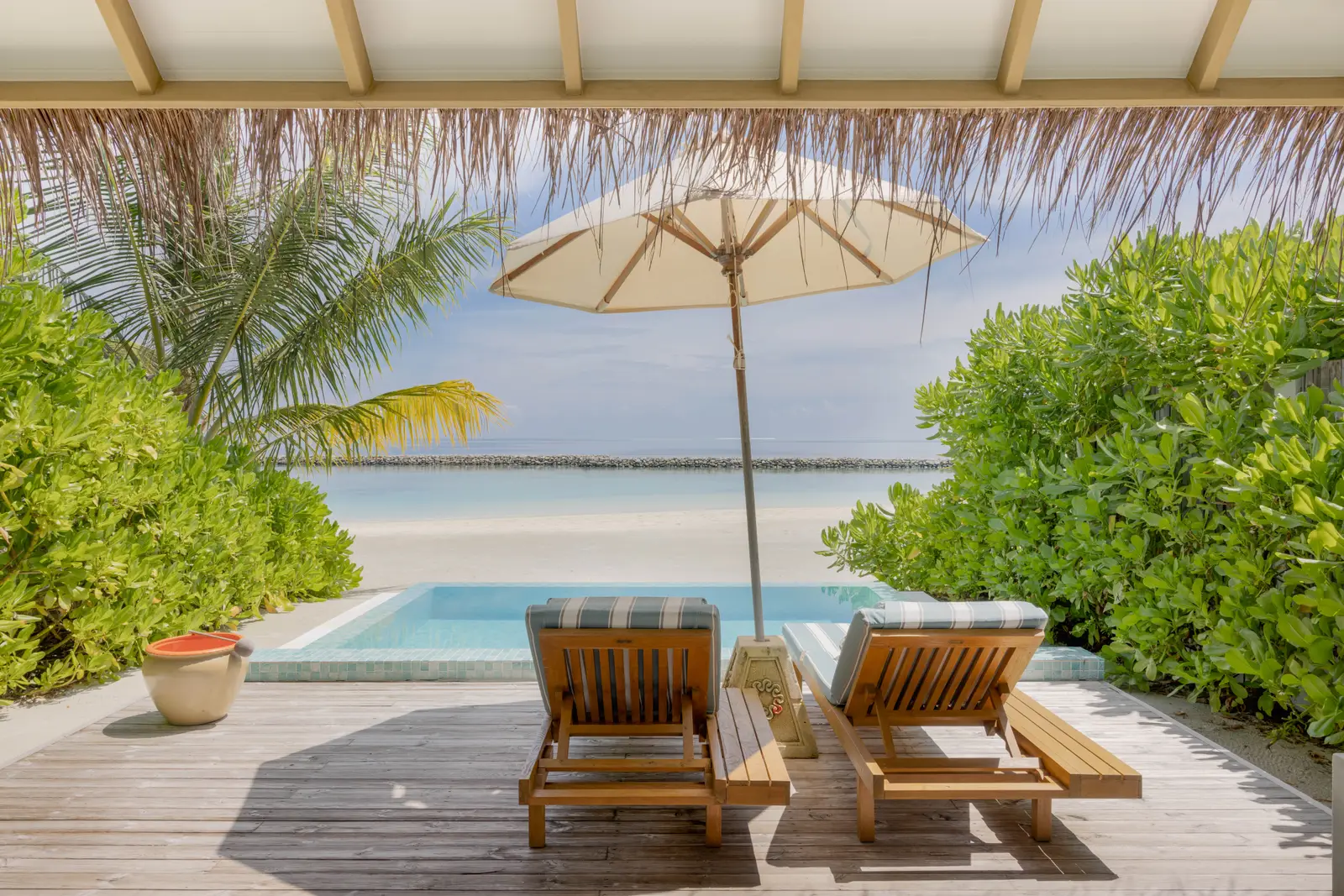 A Family Beach Villa with Pool’s deck: 2 timber loungers, the parasol and the pool towards the beach.