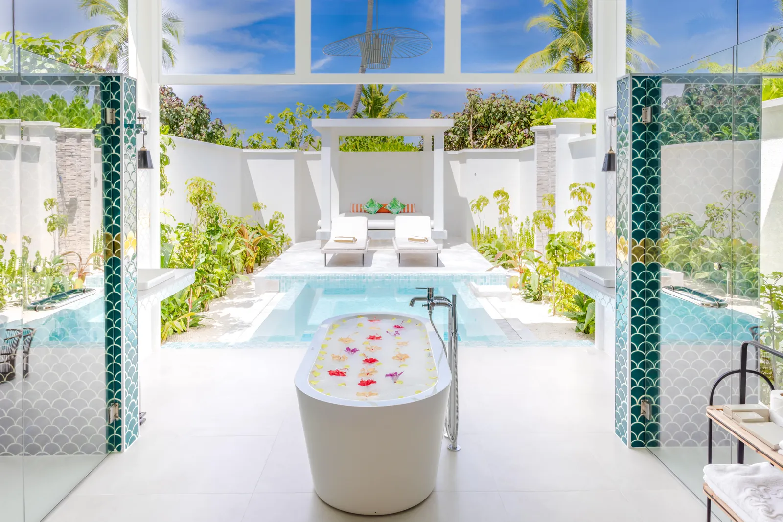 A Grand Beach Villa with Pool’s courtyard: the bath strewn with petals in front of the pool, between white walls.