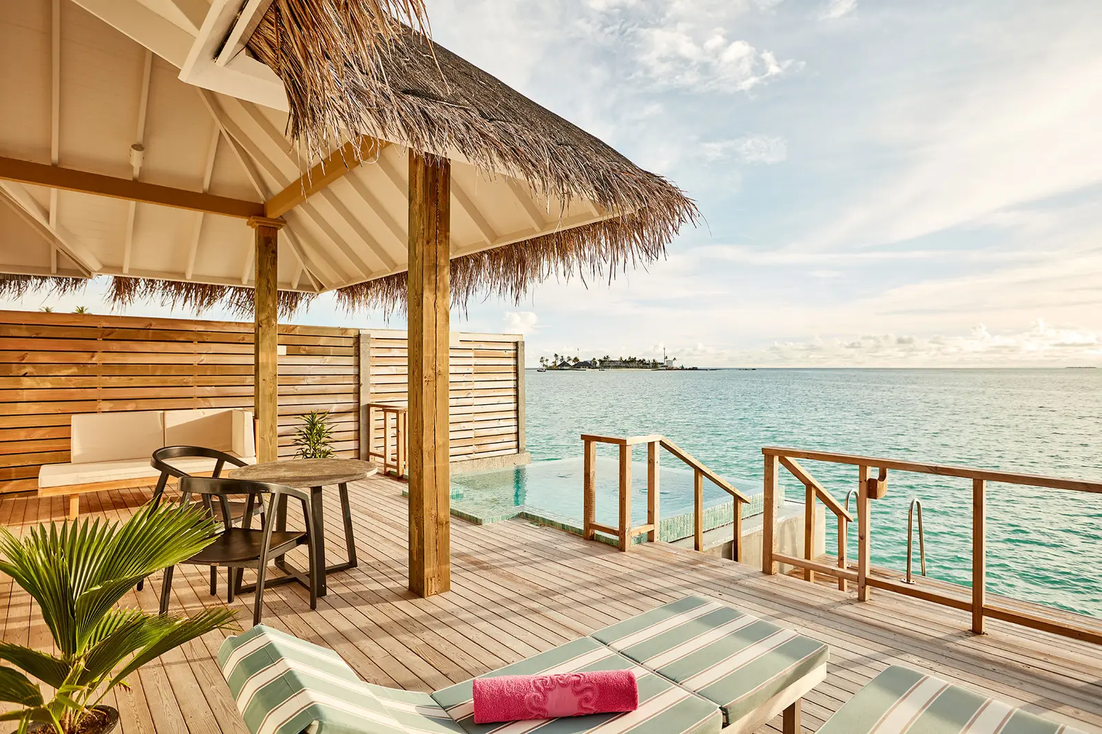 An Ocean Villa with Pool’s deck under the thatch, with its table, loungers and the ladder down to the lagoon.