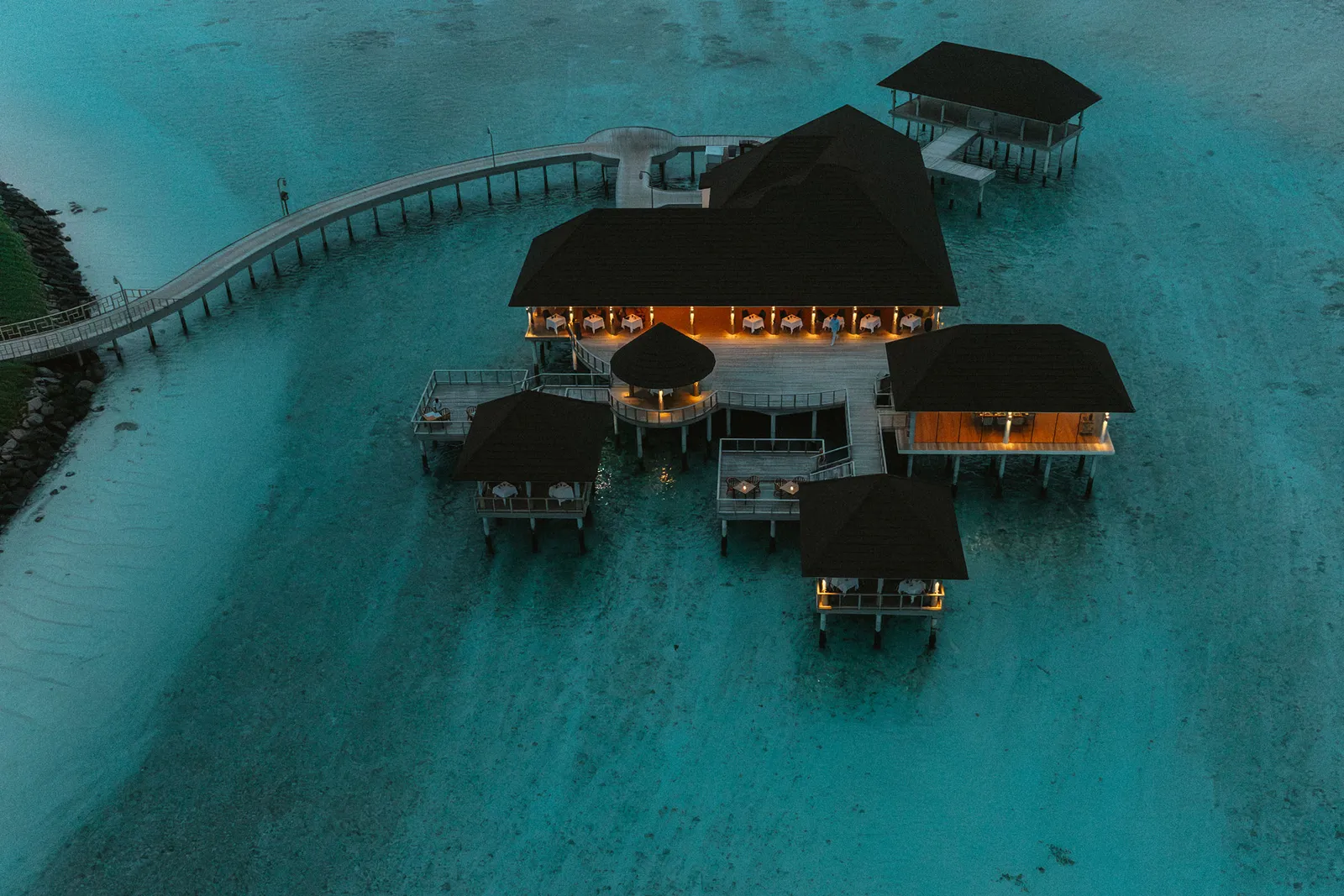 Culinarium over the water at dusk, its lights on at the end of the jetty