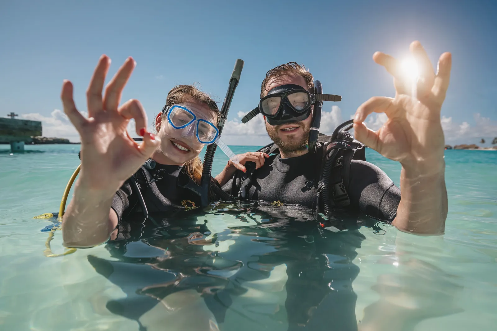 2 divers with masks in the shallows, giving the okay sign