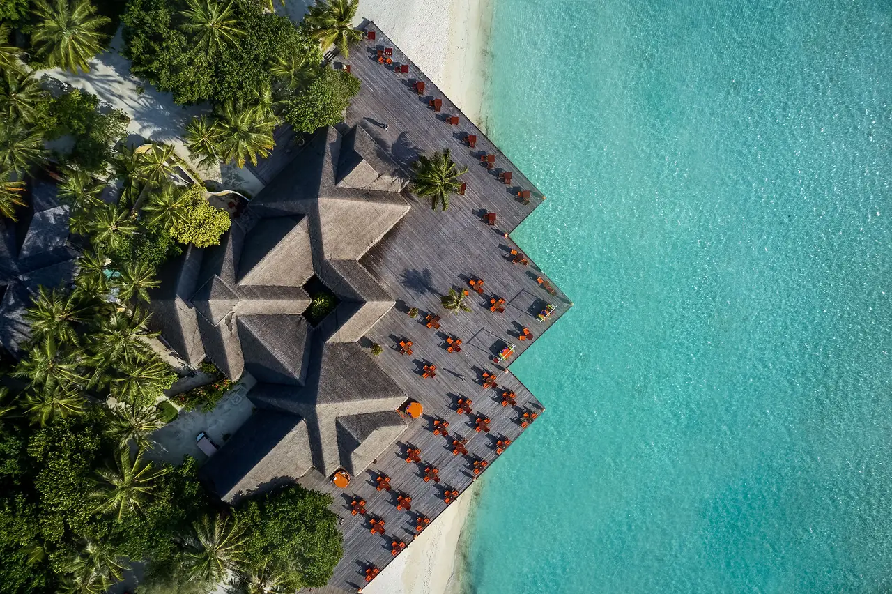 The thatched roofs of a restaurant on the shore, seen from above beside the lagoon