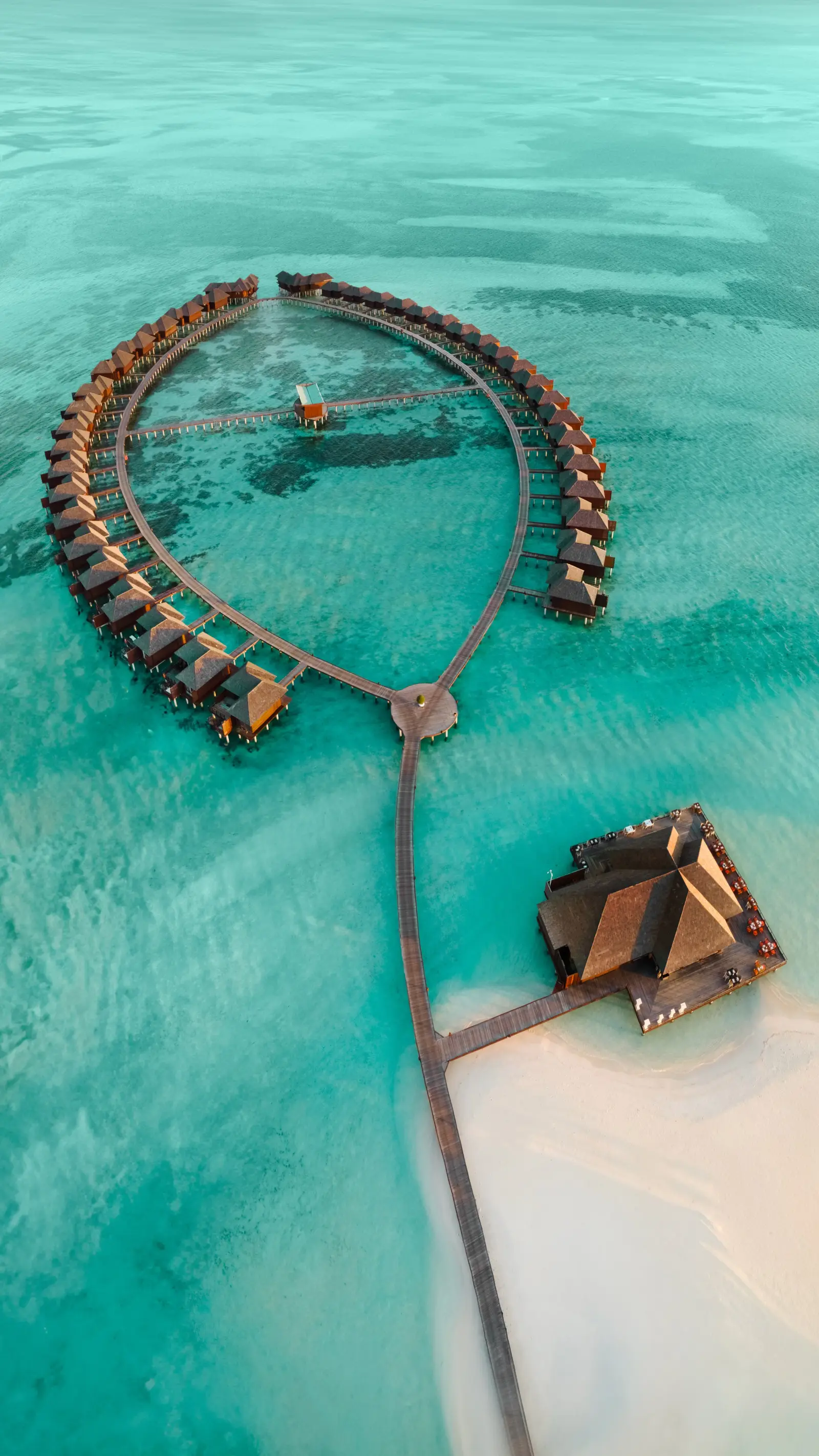 The overwater villas set in a ring from above, with the jetty and a pavilion on the lagoon
