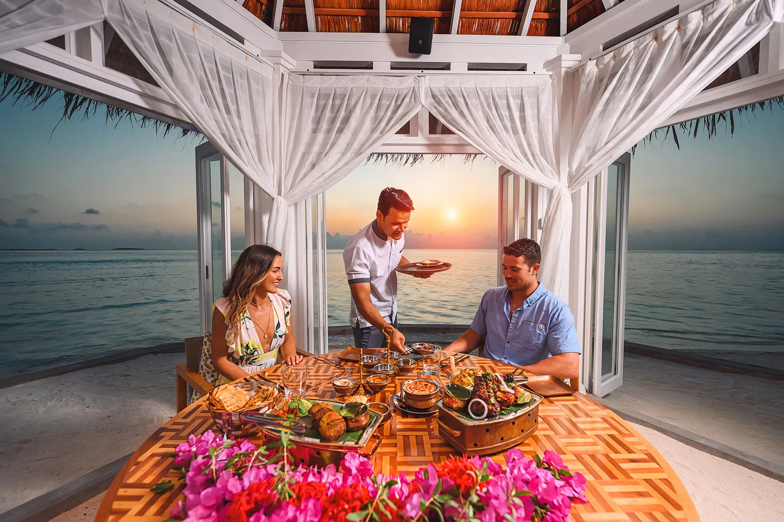 A couple dining in a Namaste cabana at sunset, served at the table