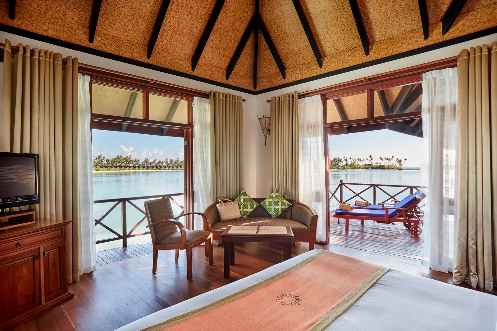 Inside a Water Villa, the bed facing the terrace over the lagoon.