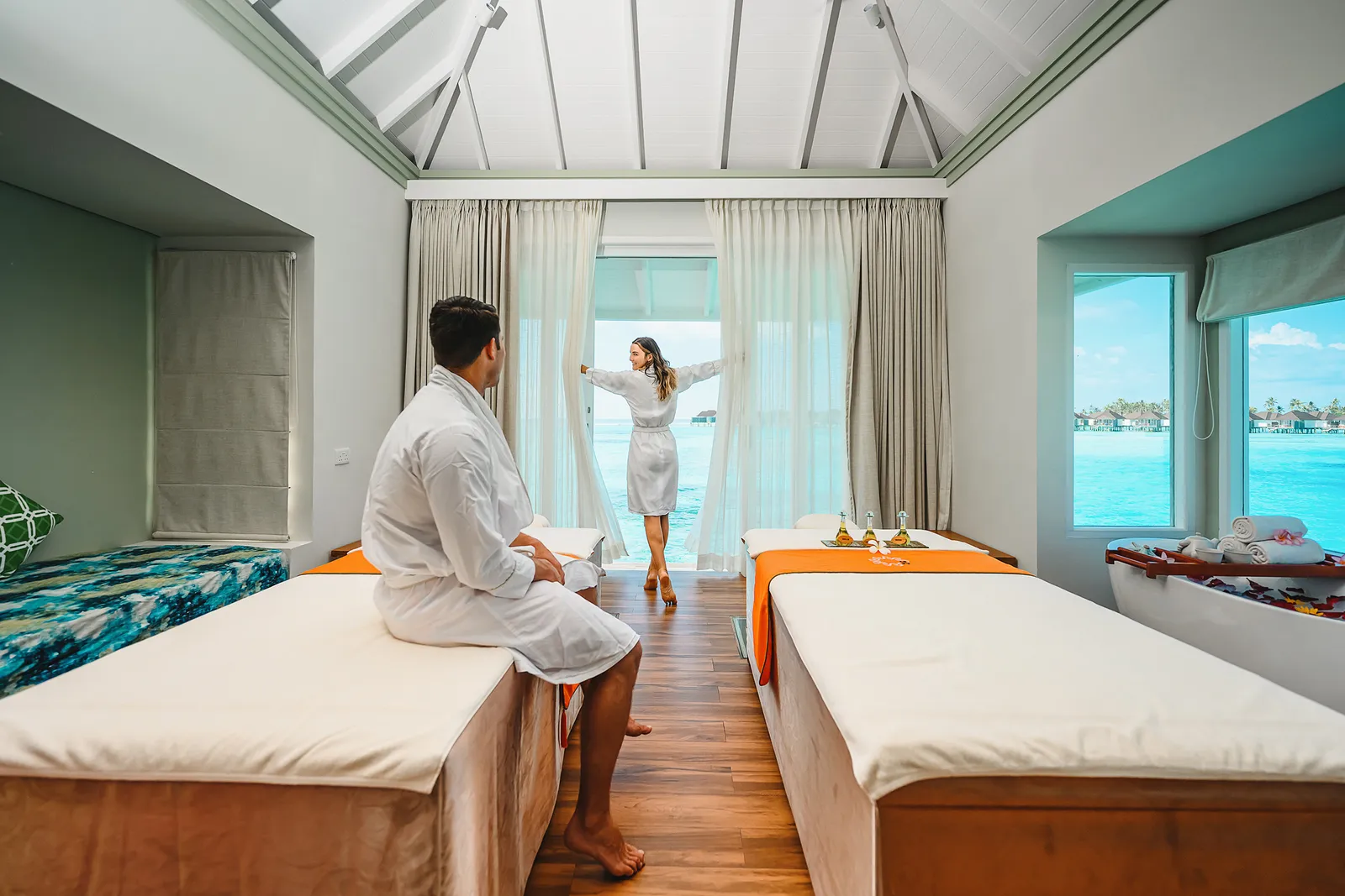 A couple in robes in the spa’s double treatment room, facing the lagoon