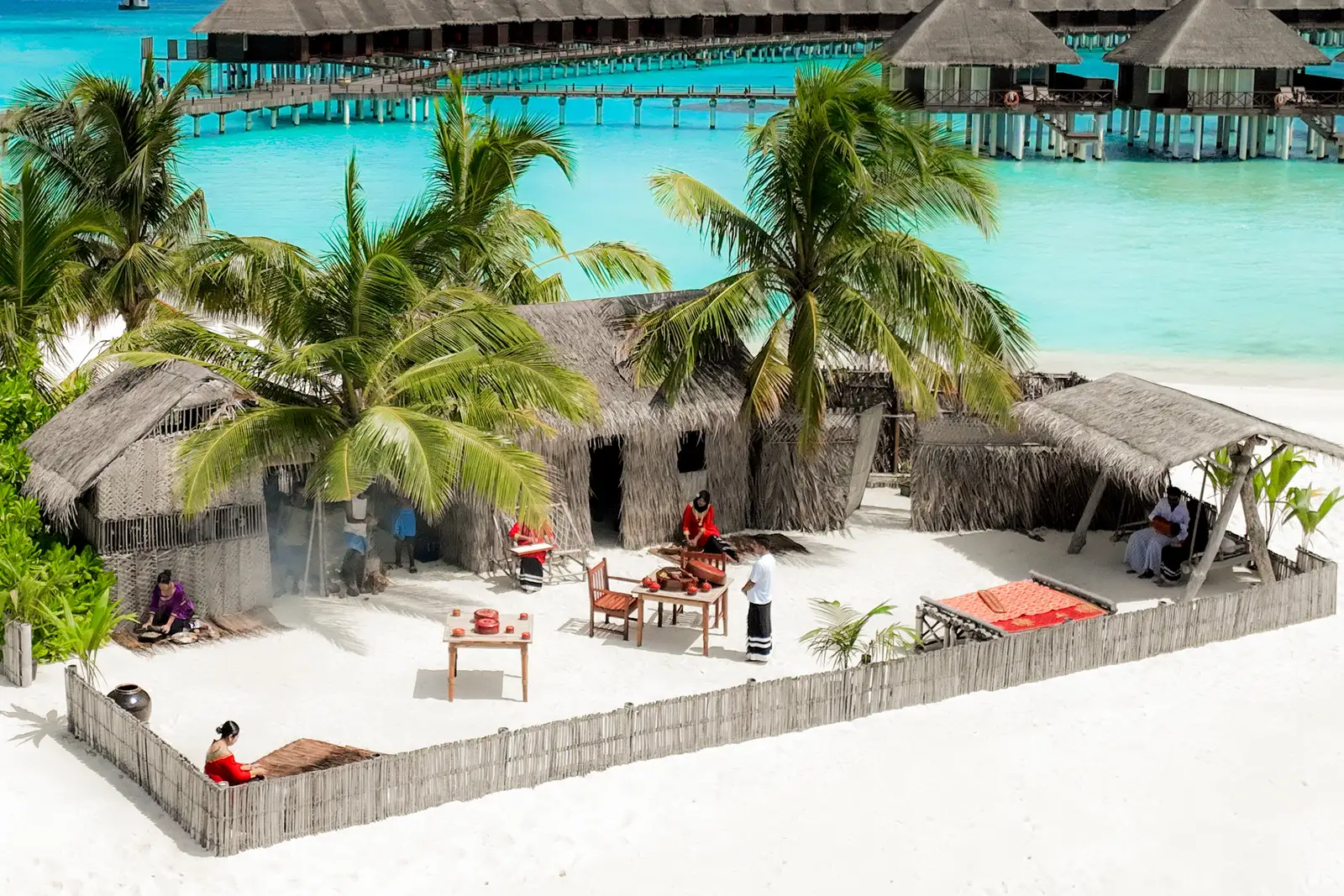Athireege from above: the thatched huts and the fence on the sand, with palms and the water villas behind.