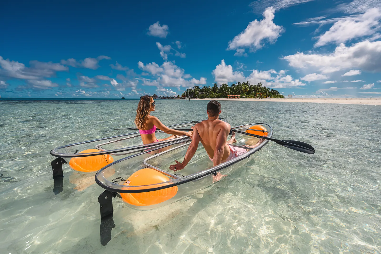 2 guests in a clear kayak on the shallow lagoon, with the island in the distance.