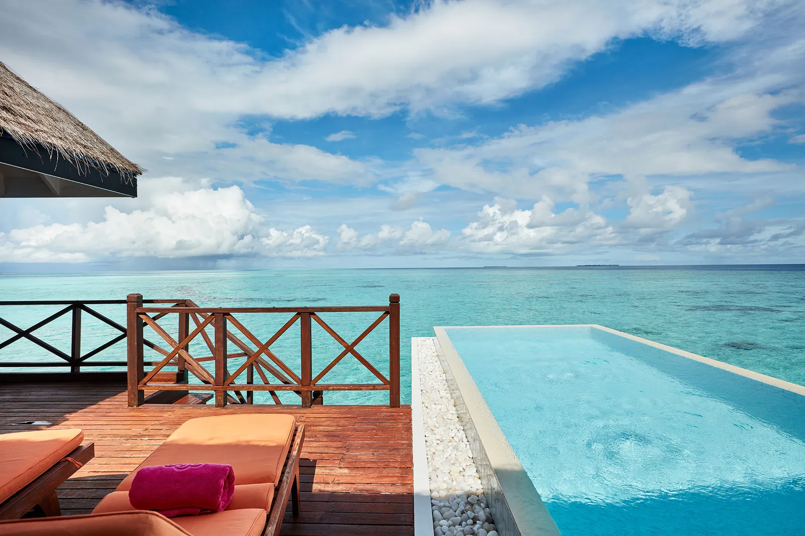 A Grand Water Villa with Pool’s infinity pool running out towards the open sea, beside the loungers.