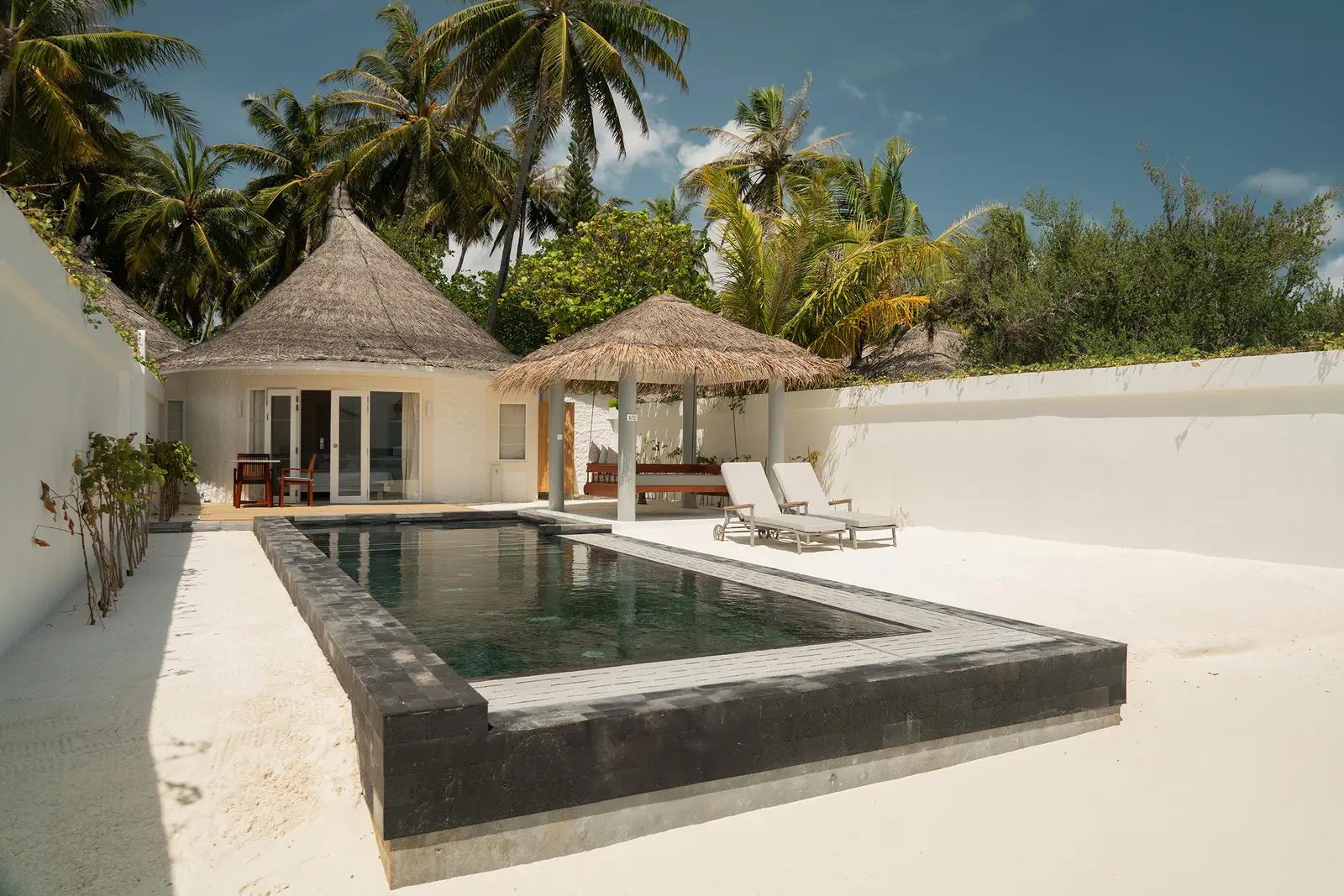 The dark-tiled pool of a Pool Beach Villa in its sandy courtyard, with the villa and the thatched pavilion behind.