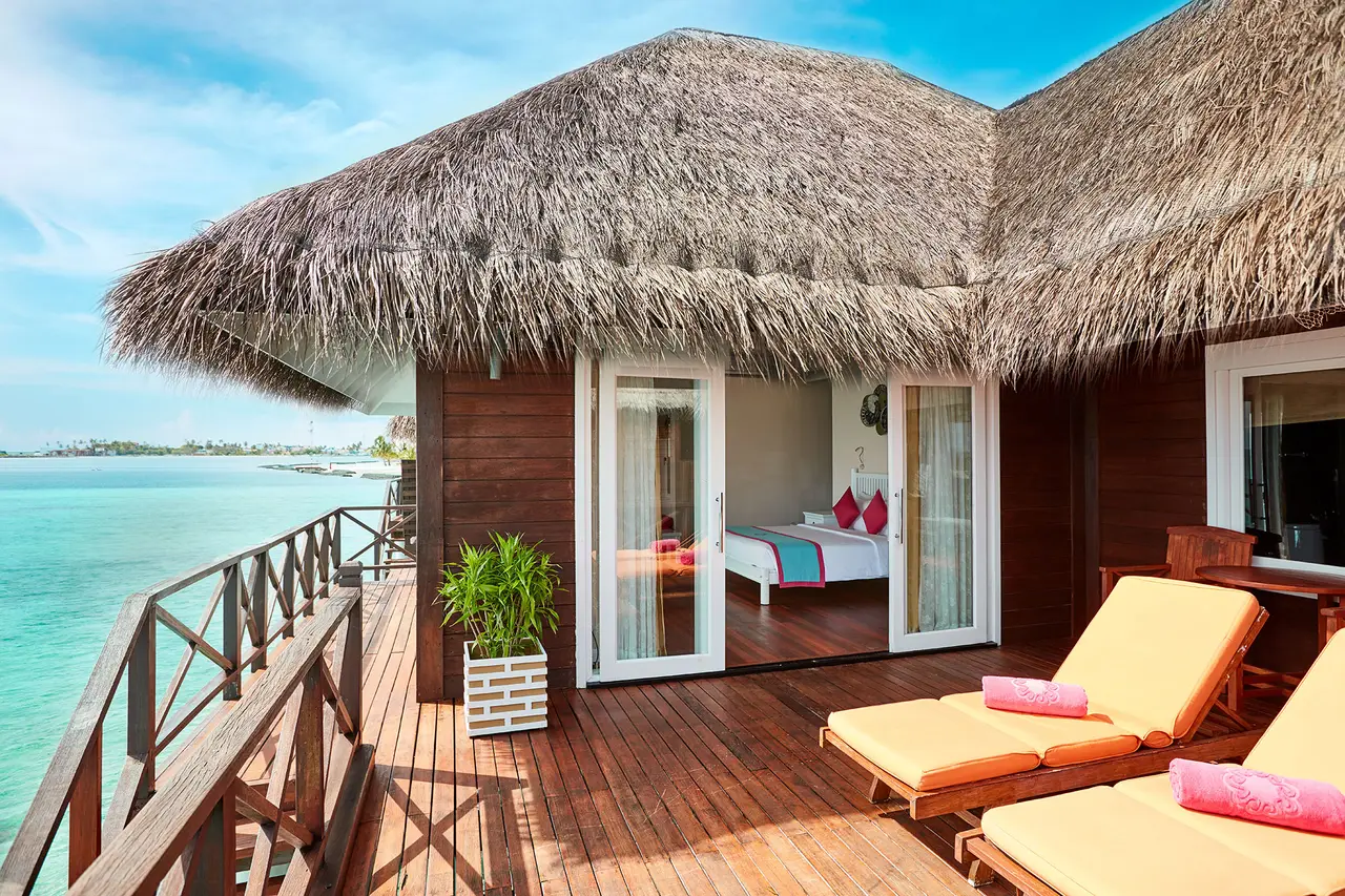 A Reef Villa’s timber deck over the water, with orange loungers, the bedroom open and the lagoon all round.